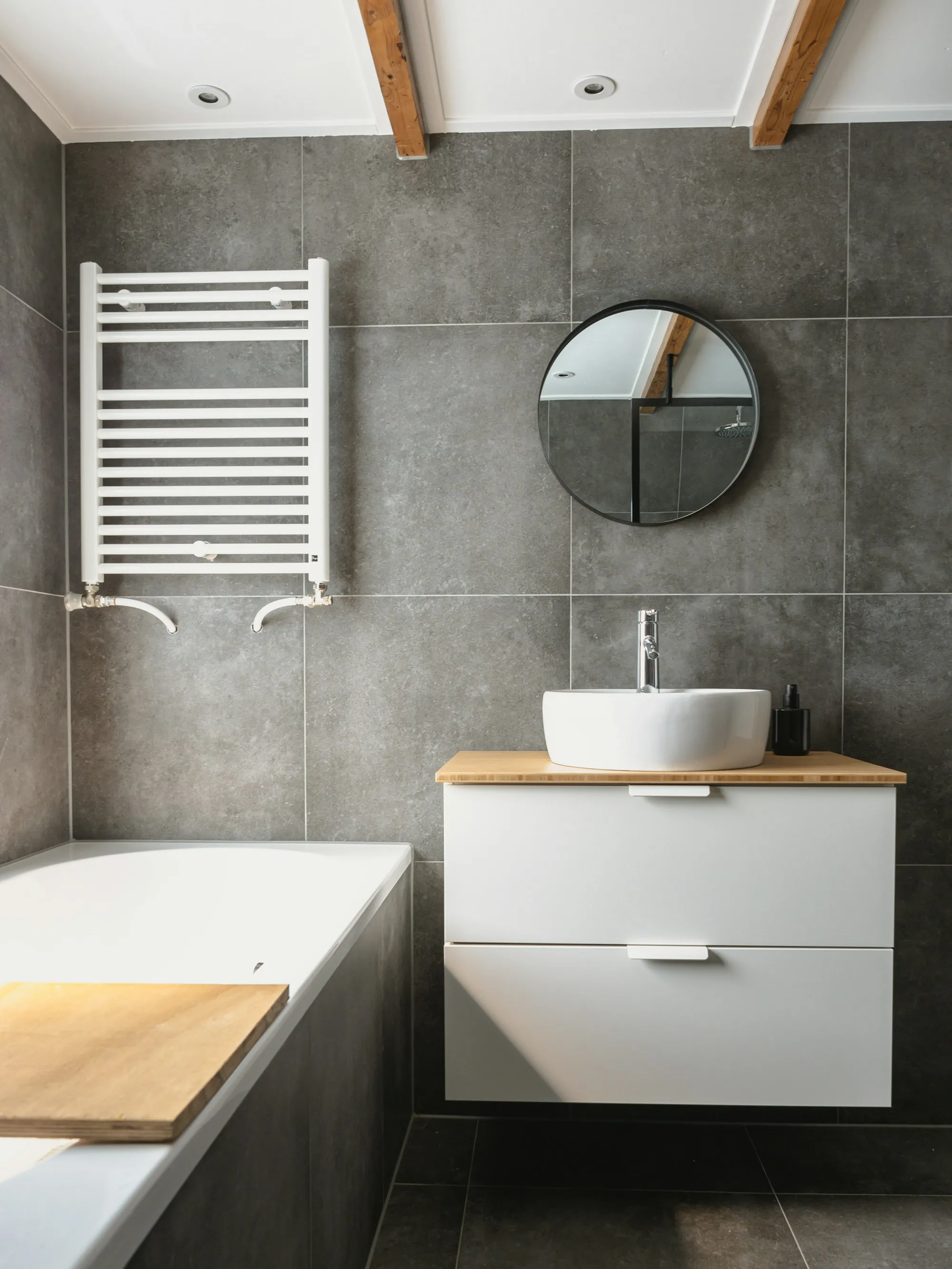 Gray-tiled bathroom with a towel warmer, round mirror and white vanity