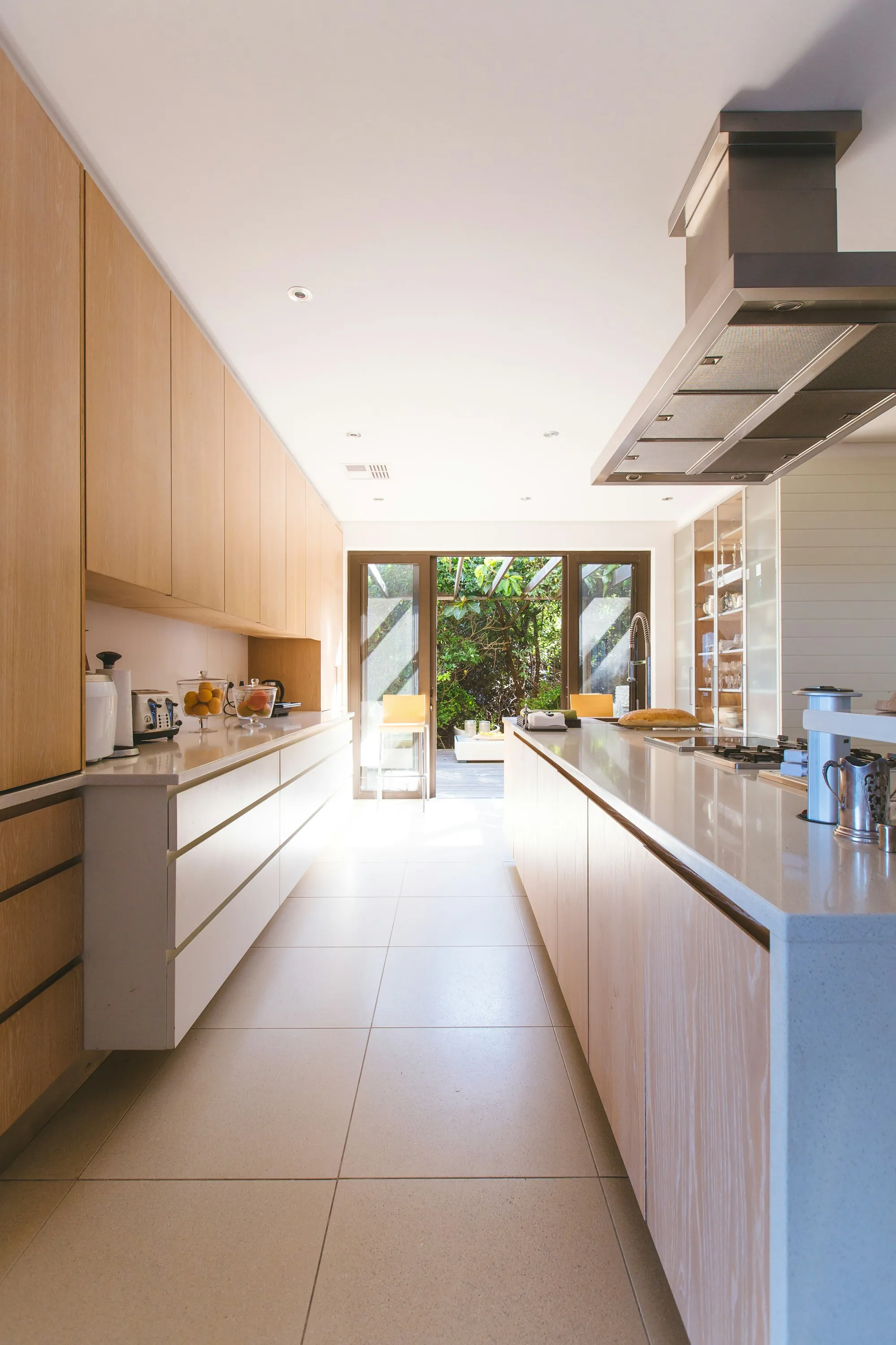 Galley kitchen with light wood cabinetry, a long island and a stainless range hood